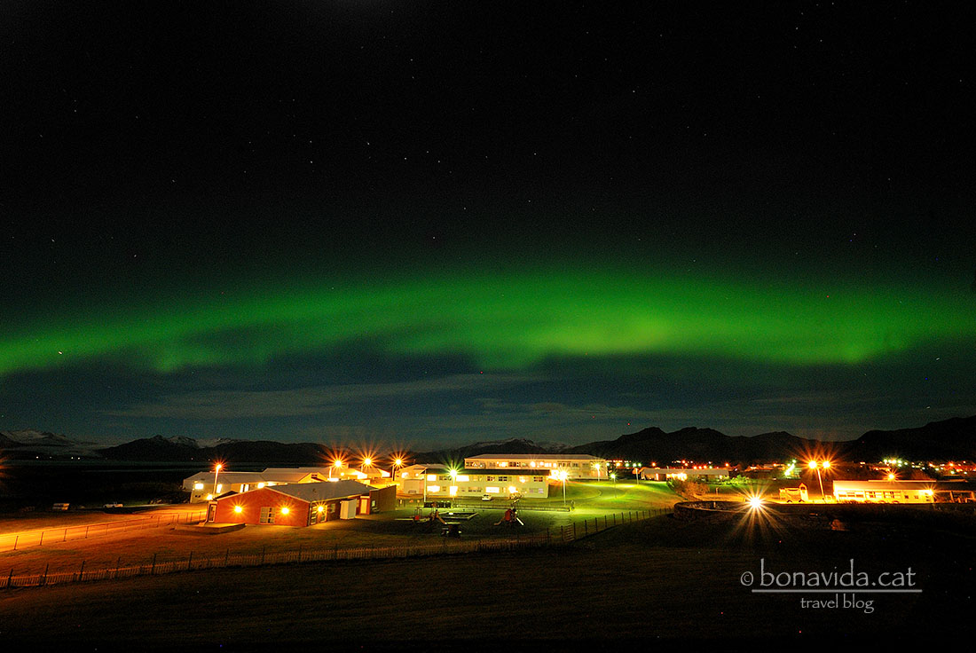 Aurora boreal sobre un paisatge nocturn amb edificis il·luminats.
