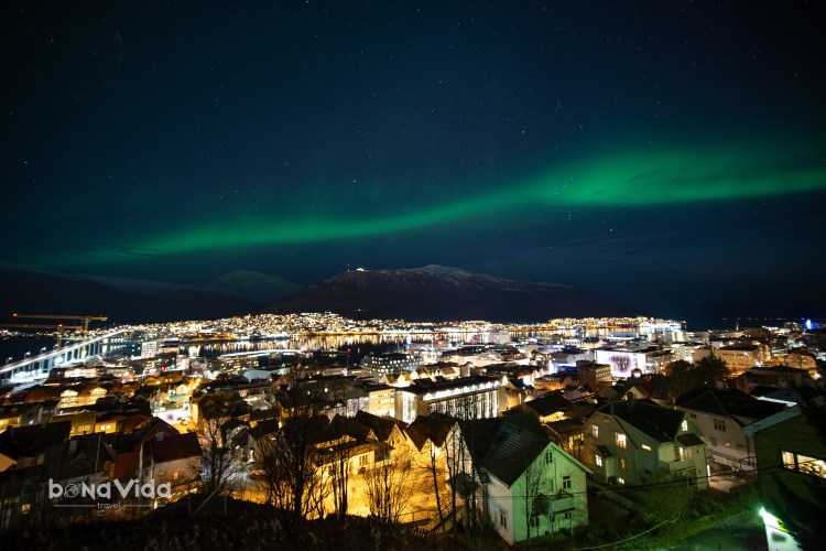 Vista nocturna d'una ciutat amb llums brillants i aurora boreal a sobre.