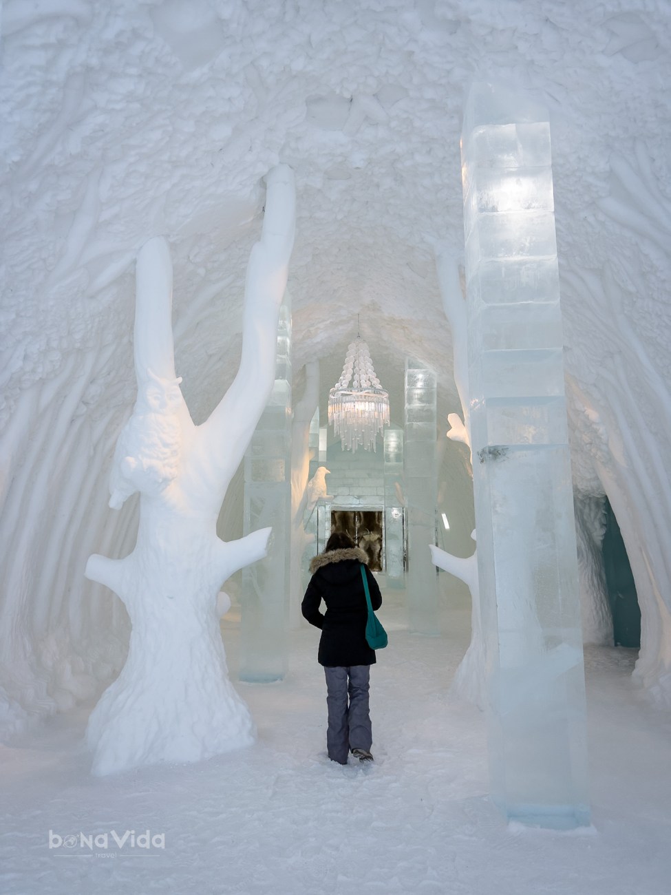 Interior d'un hotel d'entrada de gel amb escultures de neu i un candelabre penjant, on una persona camina per un passadís nevat.